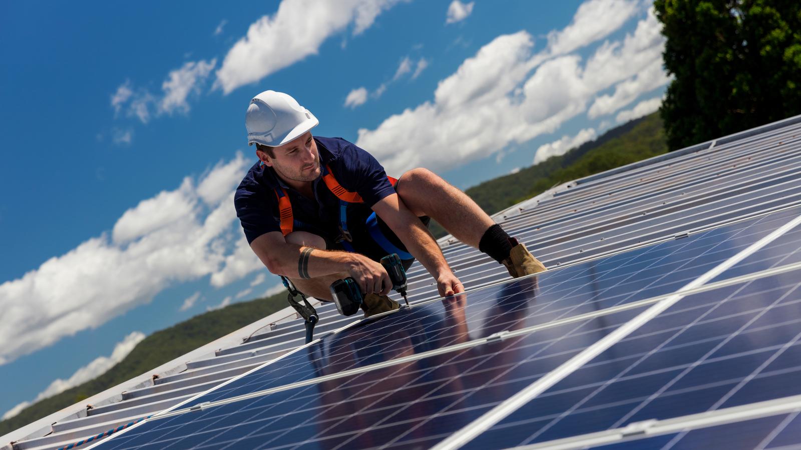 Technician installing solar panels on roof of house